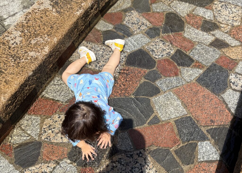 ラッシュガードを着てじゃぶじゃぶ池で水遊びする1歳児を真上から見た様子
