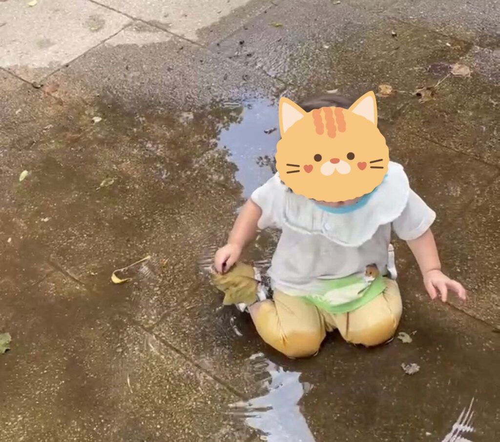 普段着のまま公園の水たまりに座り込んで遊ぶ1歳児